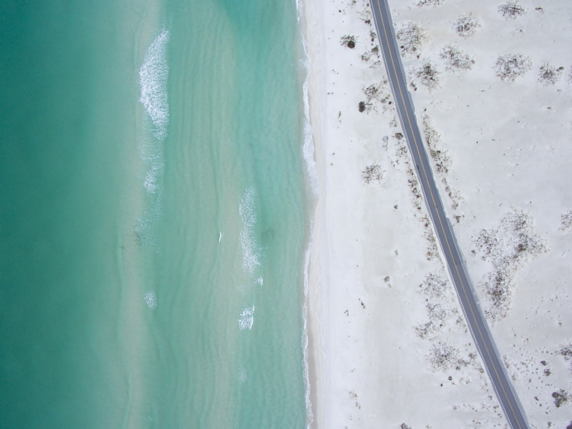 Drone photograph of emerald Gulf water rolling onto the white sand near Gulf Breeze
